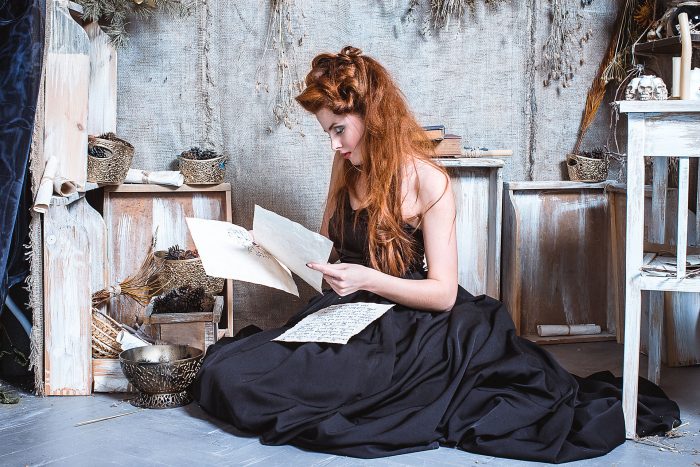 A red-haired girl in a ball gown reading pages from an old manuscript.