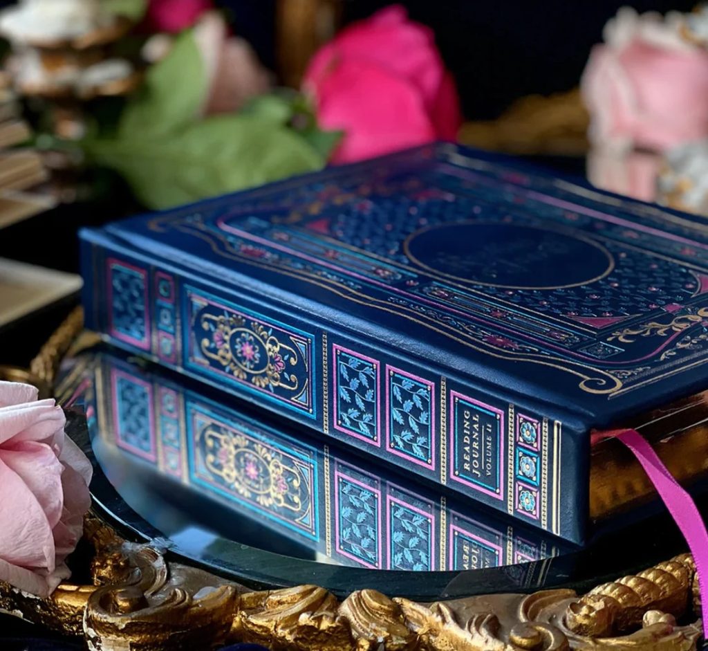 The Reading Journal from The Little Coven Collective. A royal blue hardback journal with pink and foiled gold designs.